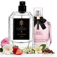 Two elegant perfume bottles on a white background, styled with flowers and strawberries. The front bottle is clear glass with a black cap and a black label reading 'THE FRAGRANCE COMPANY' and 'EAU DE PARFUM 100 ML'.