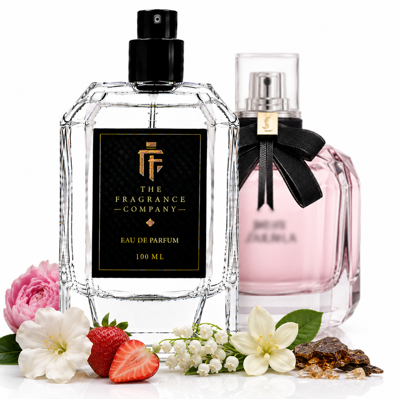 Two elegant perfume bottles on a white background, styled with flowers and strawberries. The front bottle is clear glass with a black cap and a black label reading 'THE FRAGRANCE COMPANY' and 'EAU DE PARFUM 100 ML'.