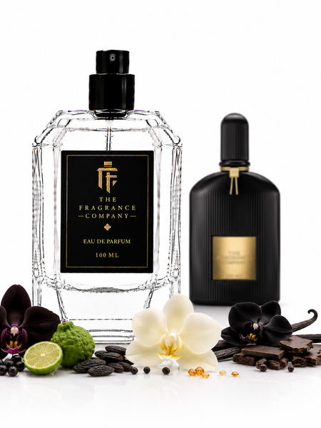 Two perfume bottles from The Fragrance Company are displayed on a white background with botanical and food props. The main bottle is a faceted clear glass bottle with a black cap and a black label featuring a gold logo and text.