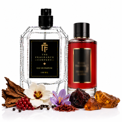 Two fragrance bottles from The Fragrance Company on a white background, surrounded by botanical and aromatic ingredients. The left bottle is a clear glass Eau de Parfum with a black cap and black label, and the right bottle is a red glass bottle with a black cap and black label.