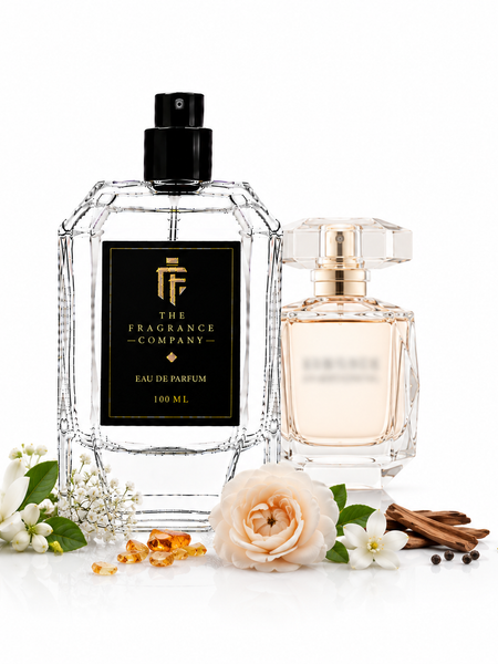 Two perfume bottles from The Fragrance Company on a white background, styled with white flowers, cinnamon sticks, and amber droplets. The larger bottle on the left is clear glass with a black label and black cap, and the smaller bottle on the right has a pale pink liquid and a gold cap.