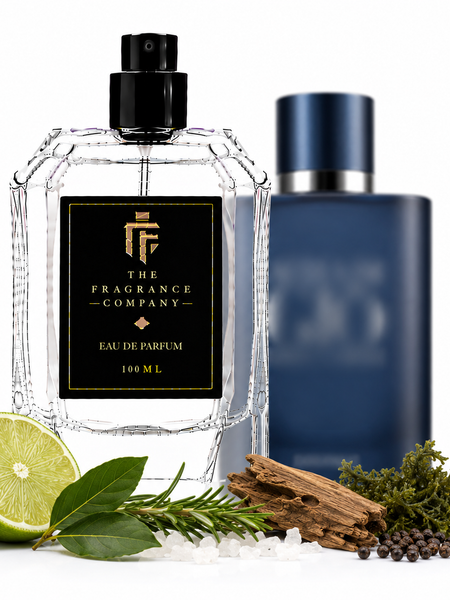 A clear glass perfume bottle labeled 'THE FRAGRANCE COMPANY' with a black cap stands in front of a dark blue bottle. The scene is styled with a lime half, rosemary sprigs, cinnamon sticks, sea salt, and peppercorns on a white background.