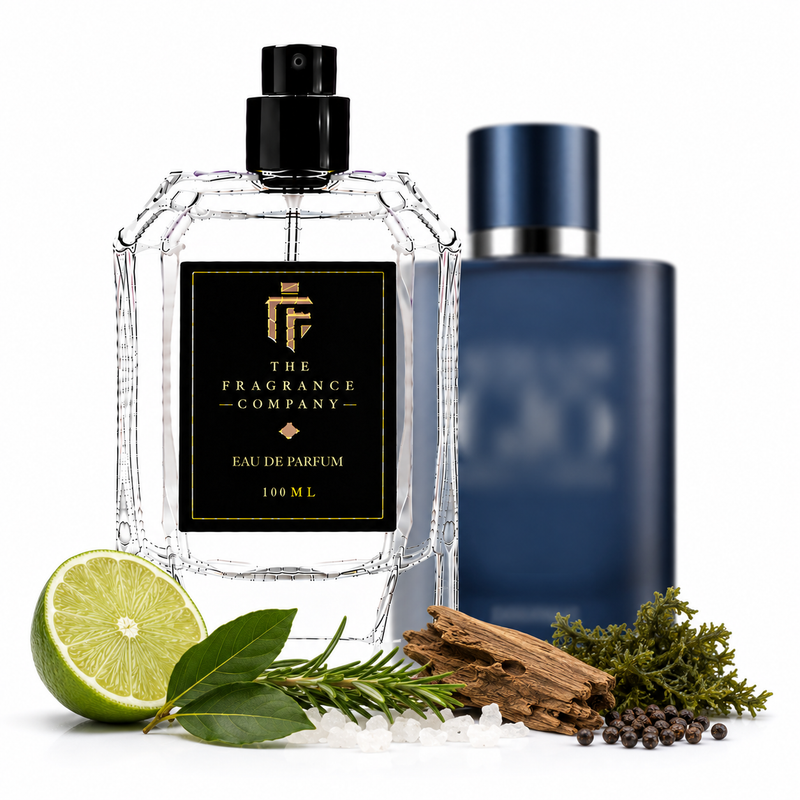 A clear glass perfume bottle labeled 'THE FRAGRANCE COMPANY' with a black cap stands in front of a dark blue bottle. The scene is styled with a lime half, rosemary sprigs, cinnamon sticks, sea salt, and peppercorns on a white background.