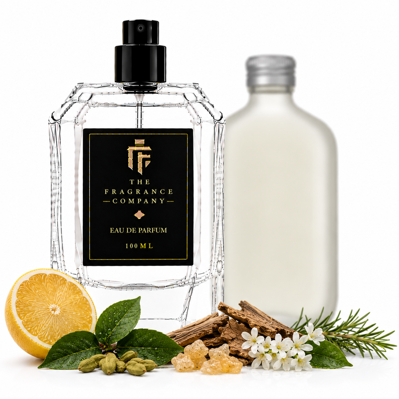A clear glass perfume bottle with a black spray top and a black label reading 'THE FRAGRANCE COMPANY' stands on a white background, styled with a sliced orange, green leaves, bark, white flowers, and a frosted bottle behind it.