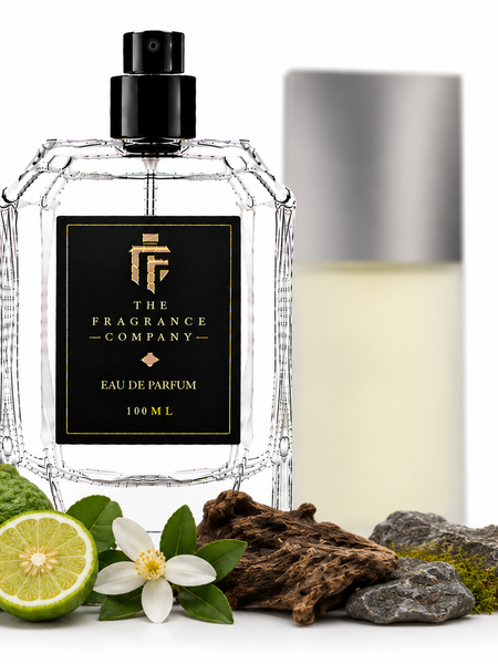 A clear glass perfume bottle with a black spray top and a black front label reading 'THE FRAGRANCE COMPANY' and 'EAU DE PARFUM 100 ML', styled with citrus, wood, moss, and rocks on a white background. A second bottle with a silver cap stands blurred in the background.