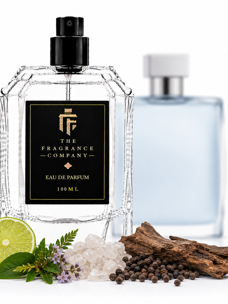 A 100ml clear glass perfume bottle with a black label and black spray cap from The Fragrance Company, styled with a light blue bottle in the background and scent ingredients including a lime slice, rosemary, sea salt, and wood pieces on a white background.