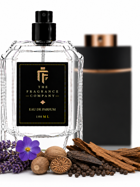 A clear glass perfume bottle with a black spray top and black label reading 'The Fragrance Company Eau De Parfum 100 ML' is centered on a white background, with decorative botanicals and spices in front and a blurred black box behind it.