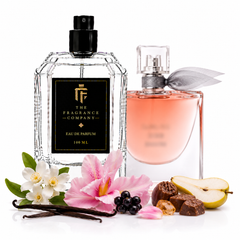Two perfume bottles from The Fragrance Company on a white background, styled with floral and fruit props including white and pink flowers, vanilla beans, blackberries, and pear slices. The left bottle is clear glass with a black label and black spray top, and the right bottle is a soft pink glass spray bottle with a gray ribbon.