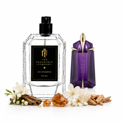 A 100 ml clear faceted glass perfume bottle with a black label and black spray cap from The Fragrance Company, styled with white flowers, amber crystals, and cinnamon sticks next to a purple Vessel perfume bottle on a white background.