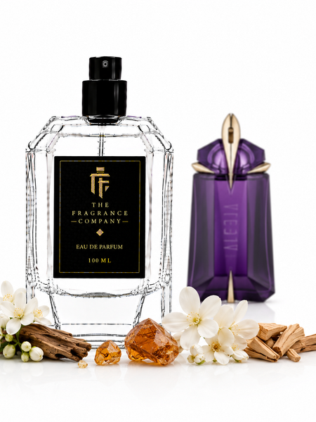 A 100 ml clear faceted glass perfume bottle with a black label and black spray cap from The Fragrance Company, styled with white flowers, amber crystals, and cinnamon sticks next to a purple Vessel perfume bottle on a white background.