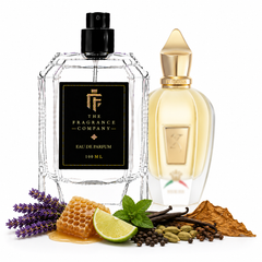 Two perfume bottles from The Fragrance Company are displayed on a white background with scent ingredients arranged around the base. The foreground bottle is clear glass with a black label and black spray top, while the background bottle is translucent with a pale yellow liquid and gold cap.