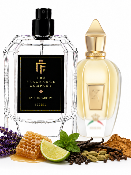 Two perfume bottles from The Fragrance Company are displayed on a white background with scent ingredients arranged around the base. The foreground bottle is clear glass with a black label and black spray top, while the background bottle is translucent with a pale yellow liquid and gold cap.