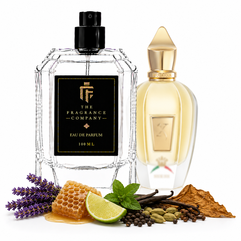 Two perfume bottles from The Fragrance Company are displayed on a white background with scent ingredients arranged around the base. The foreground bottle is clear glass with a black label and black spray top, while the background bottle is translucent with a pale yellow liquid and gold cap.