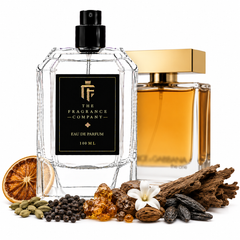 Two perfume bottles from The Fragrance Company on a white background, surrounded by scent ingredients including a dried orange slice, cardamom, black peppercorns, amber crystals, a white flower, and wood bark. One bottle is clear glass with a black spray top and black label, and the other is a gold-toned bottle with amber liquid.