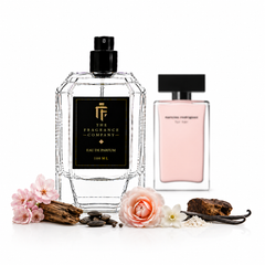 Two perfume bottles on a white background, one large faceted clear bottle labeled 'The Fragrance Company' and one smaller pale pink bottle labeled 'marine migdaliuk For Her'. Decorative flowers, vanilla pods, and spices are arranged around the bottles.
