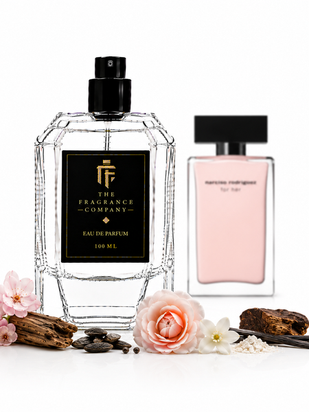 Two perfume bottles on a white background, one large faceted clear bottle labeled 'The Fragrance Company' and one smaller pale pink bottle labeled 'marine migdaliuk For Her'. Decorative flowers, vanilla pods, and spices are arranged around the bottles.