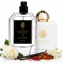 Two perfume bottles from The Fragrance Company on a white background, styled with white roses, vanilla beans, and amber beads. The foreground bottle is a faceted clear glass bottle with a black cap and a black label featuring gold lettering.