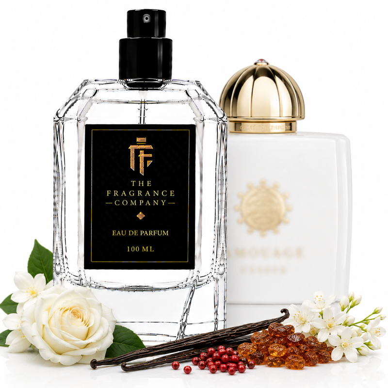 Two perfume bottles from The Fragrance Company on a white background, styled with white roses, vanilla beans, and amber beads. The foreground bottle is a faceted clear glass bottle with a black cap and a black label featuring gold lettering.