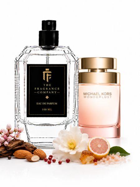 Two perfume bottles on a white background: a large clear glass bottle with a black pump and black label reading The Fragrance Company Eau de Parfum 100 ML, and a Michael Kors Wonderlust bottle with a gold cap and pale pink body. Decorative flowers, nuts, spices, and citrus pieces are arranged around the bottles.