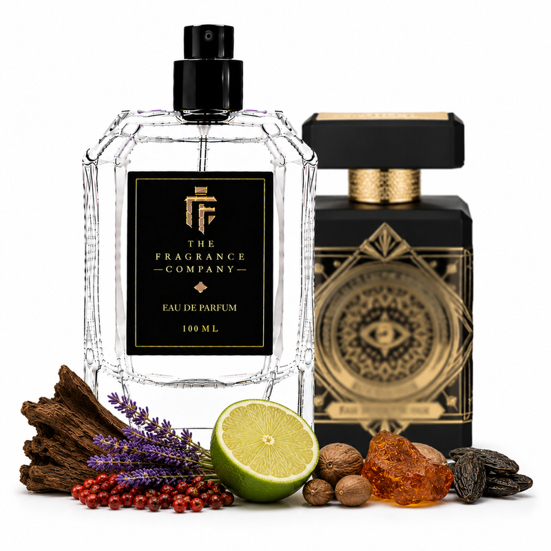 A clear faceted perfume bottle labeled 'The Fragrance Company' stands in front of a black-and-gold branded box, with botanical and spice ingredients arranged around the base on a white background.