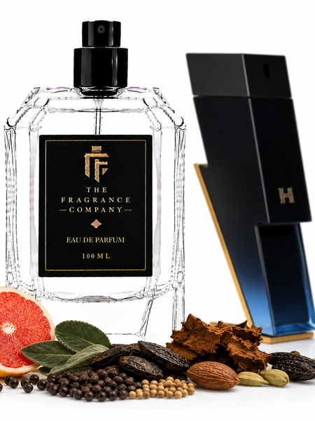 A 100 mL clear glass perfume bottle with a black spray top and a black front label reading 'THE FRAGRANCE COMPANY' and 'EAU DE PARFUM 100 ML', shown on a white background with citrus, spices, and bark props. A tall black-and-blue geometric box stands behind the bottle.