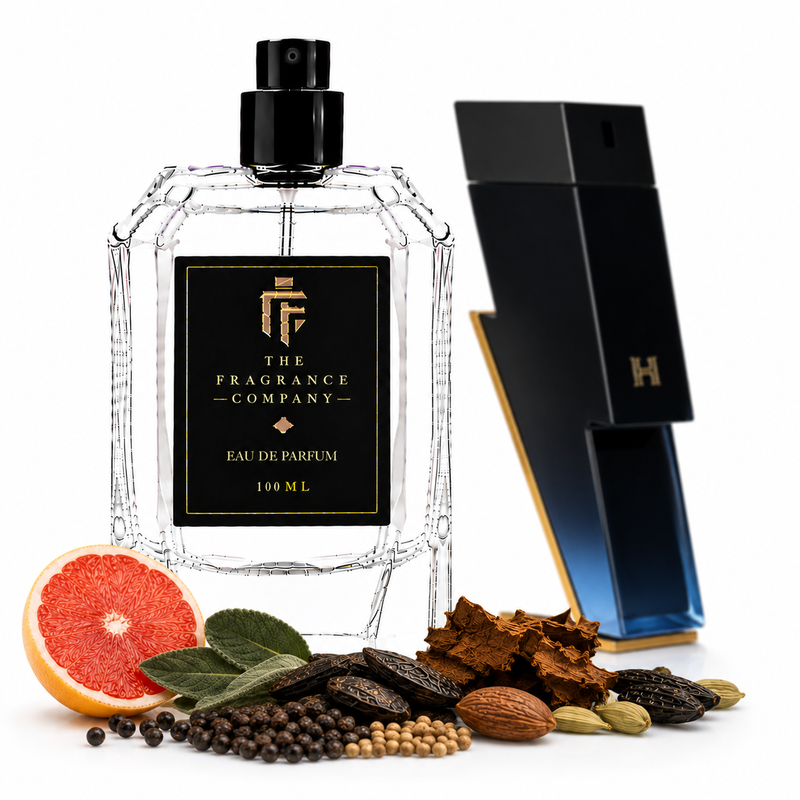 A 100 mL clear glass perfume bottle with a black spray top and a black front label reading 'THE FRAGRANCE COMPANY' and 'EAU DE PARFUM 100 ML', shown on a white background with citrus, spices, and bark props. A tall black-and-blue geometric box stands behind the bottle.