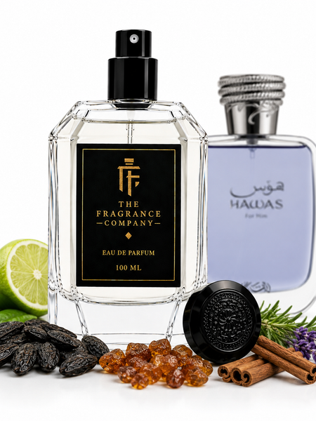 Two perfume bottles displayed on a white background with scent ingredients around them. The front bottle is a faceted clear glass spray bottle labeled 'THE FRAGRANCE COMPANY' with a black label and black spray top.